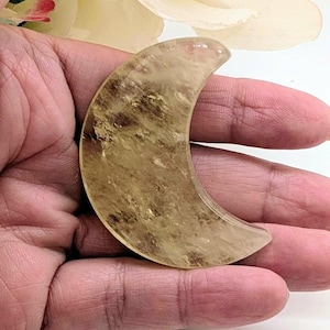 May include: A crescent moon-shaped carving made of translucent, golden-yellow citrine crystal. The stone features natural internal inclusions and a smooth, polished surface. The number 1 is printed in black in the bottom right corner.