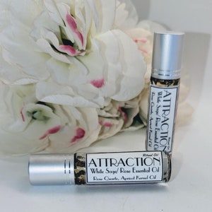 May include: Two silver roller bottles with white labels that read "ATTRACTION Ritual Oil White Sage/Rose Essential Oil Rose Quartz, Apricot Kernel Oil".