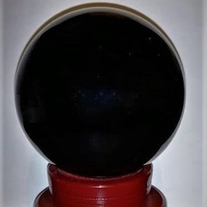 May include: A large, glossy black crystal ball rests on a vibrant red, tiered stand. The spherical orb reflects light, creating a mysterious appearance. This decorative piece is suitable for home decor or spiritual practices.