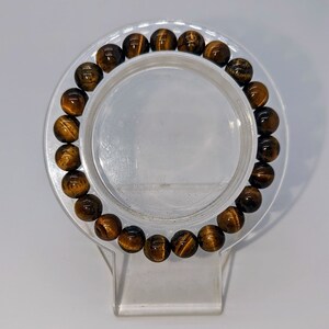 May include: A brown and gold tiger's eye beaded bracelet on a clear display stand.