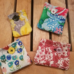 May include: Four small fabric pouches with floral patterns and buttons. The pouches are made of different fabrics with various colors and designs, including red, pink, blue, green, yellow, and gray.