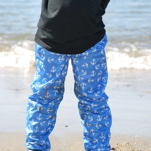 May include: A child wearing blue pants with a white anchor pattern. The pants are pulled up to the waist and the child is wearing black boots.