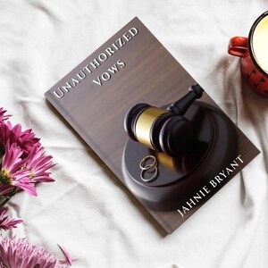 May include: A book titled "UNAUTHORIZED VOWS" by Jahnie Bryant. The cover features a gavel, wedding rings, and a wooden background. A red mug with a candle sits to the right, and pink flowers are in the lower left corner.