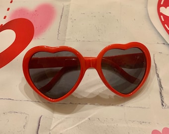 May include: Red heart-shaped sunglasses with dark lenses.