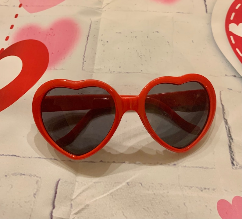 May include: Red heart-shaped sunglasses with dark lenses.