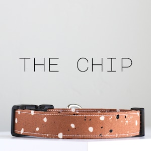 May include: A brown dog collar with white and black spots. The collar has a black buckle and is made of fabric. The text "THE CHIP" is printed above the collar.