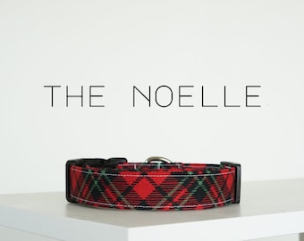 Op de afbeelding: Rode en zwarte geruite hondenriem met witte stiksels en een zwarte gesp. De riem heeft de tekst "THE NOELLE" erboven gedrukt.