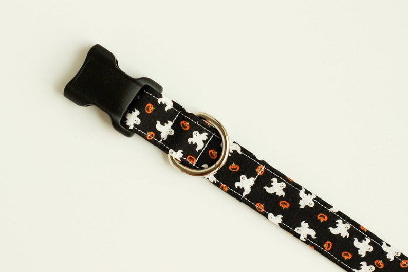 May include: Black dog collar with a Halloween print featuring white ghosts and orange pumpkins.