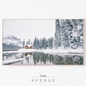 May include: A snowy winter scene with a cabin nestled in a forest of snow-covered pine trees. The cabin is reflected in the still water of a lake.