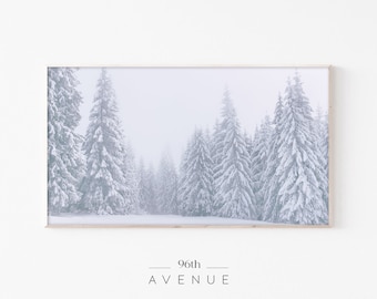 Könnte beinhalten: Ein gerahmtes Foto einer verschneiten Waldszene mit hohen, schneebedeckten Kiefern. Die Bäume sind vor einem weißen, nebligen Hintergrund silhouettiert. Das Bild ist in einem hellen Holzrahmen gerahmt.