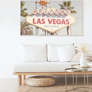 May include: A vintage-style photograph of the iconic "Welcome to Fabulous Las Vegas" sign with palm trees in the background. The sign is lit up with neon lights and the sky is a light blue. The image is perfect for a retro-themed home decor.
