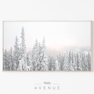 May include: A framed photograph of a snowy forest scene with tall evergreen trees covered in white snow. The background is a soft, hazy pink and white.