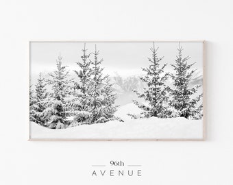 Könnte beinhalten: Schwarzweißfotografie einer schneebedeckten Berglandschaft mit einer Gruppe von Kiefern im Vordergrund. Die Bäume sind mit Schnee bedeckt und die Berge sind im Hintergrund. Das Bild ist in einem weißen Rahmen gerahmt.