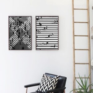 K&ouml;nnte beinhalten: Zwei schwarz-wei&szlig;e gerahmte Drucke mit abstrakten geometrischen Mustern. Die Drucke h&auml;ngen an einer wei&szlig;en Wand &uuml;ber einem schwarzen Ledersessel mit einem schwarz-wei&szlig;en gemusterten Kissen. Eine Holzleiter lehnt an der Wand rechts von den Drucken.