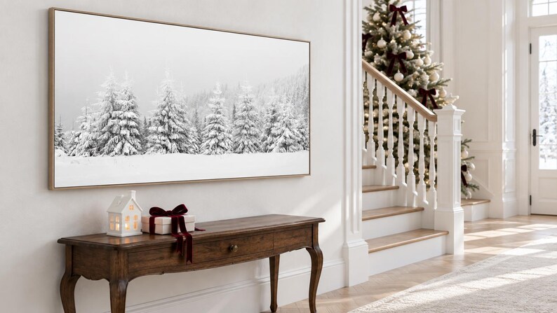 K&ouml;nnte beinhalten: Ein rechteckiger Wandkunstdruck mit einer schwarz-wei&szlig;en Winterlandschaft aus schneebedeckten Tannenb&auml;umen. Der Druck ist in einem hellen Holzrahmen gefasst und an einer wei&szlig;en Wand &uuml;ber einem dunklen Holzkonsolentisch angebracht.