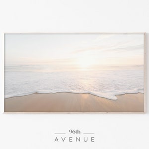 May include: A photograph of a beach scene with white foamy waves crashing on the shore. The sand is a light beige color and the sky is a soft, pale blue. The sun is shining brightly, casting a warm glow over the scene. The text "96th AVENUE" is printed at the bottom of the image.