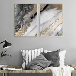 Puede incluir: Dos impresiones de arte abstracto con fondo blanco y detalles dorados y grises. Las impresiones est&aacute;n enmarcadas en un marco fino de madera clara.