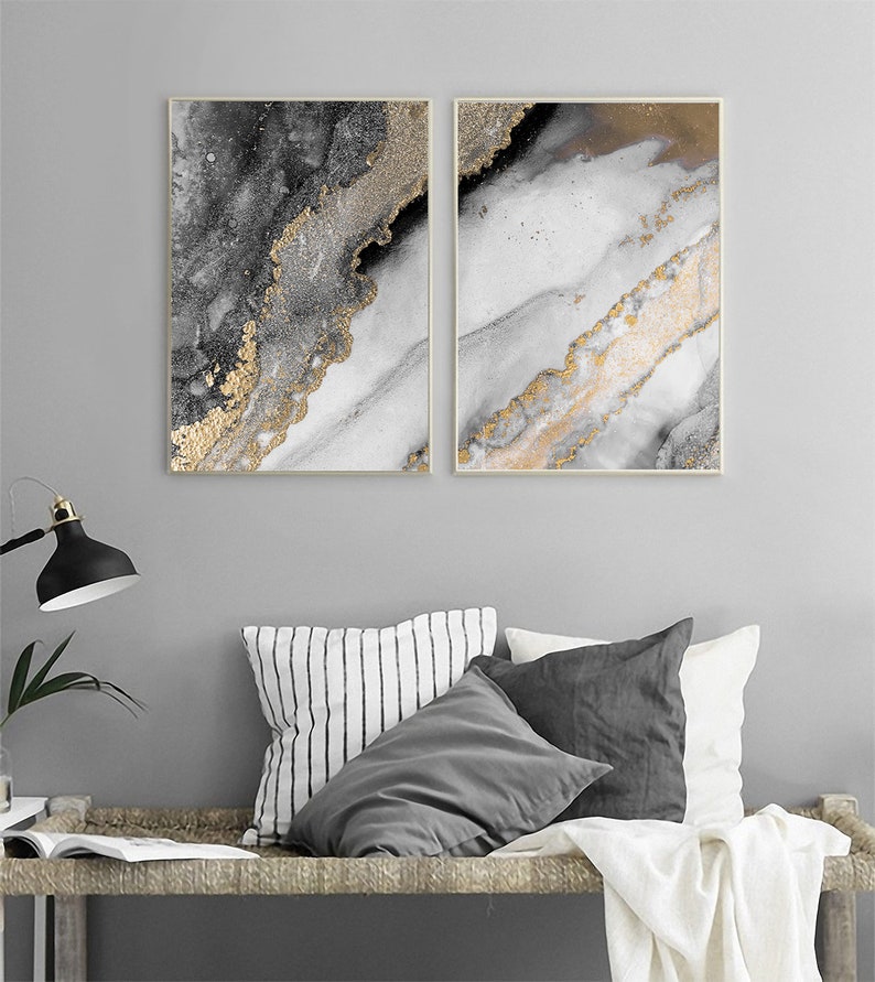 Puede incluir: Dos impresiones de arte abstracto con fondo blanco y detalles dorados y grises. Las impresiones est&aacute;n enmarcadas en un marco fino de madera clara.