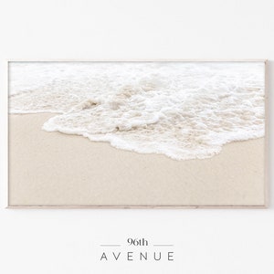 May include: A close-up of white foamy ocean waves crashing on a sandy beach. The waves are breaking and creating a soft, white texture on the sand.