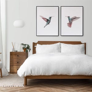 Może przedstawiać: Białe ł&oacute;żko z drewnianym stelażem i białą pościelą. Nad ł&oacute;żkiem na ścianie wiszą dwa oprawione obrazy z kolibrami.