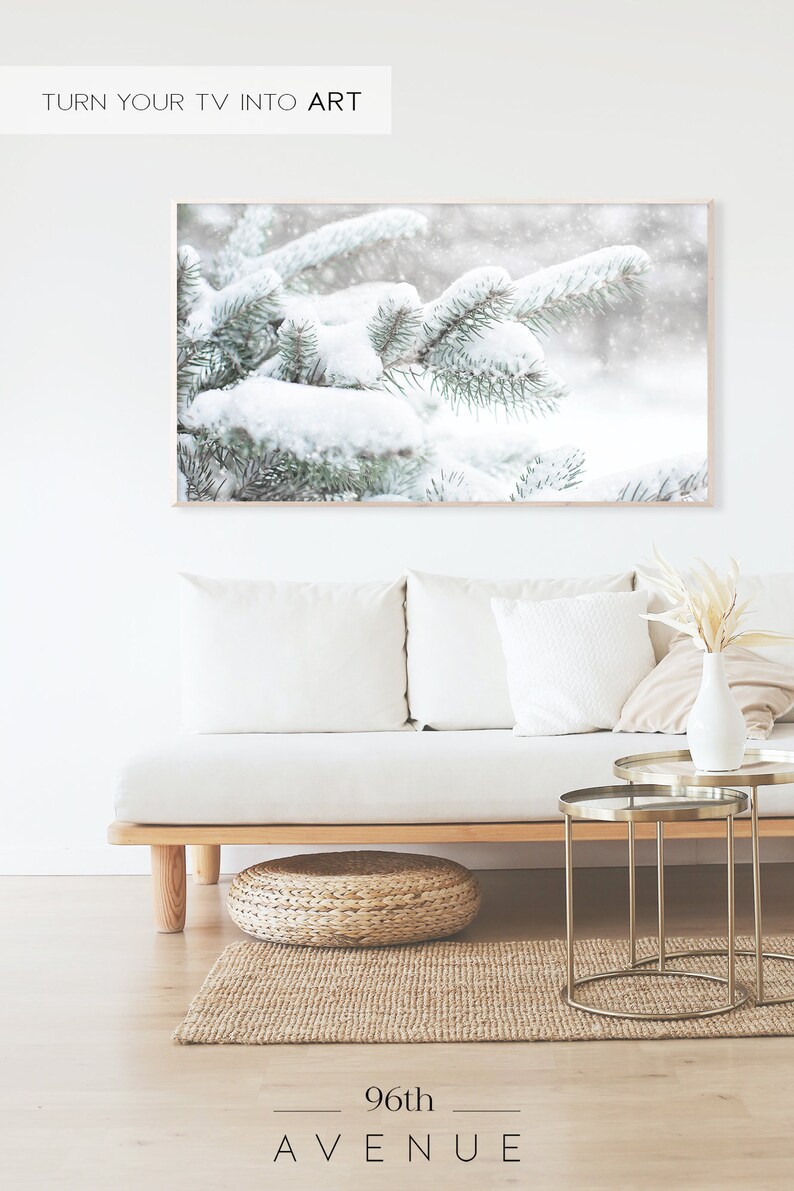 May include: A snowy winter scene with pine branches covered in white snow. The branches are in focus, while the background is blurred and out of focus. The image is framed in a light wood frame.