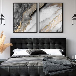 Puede incluir: Dos impresiones de arte abstracto con pintura negra, blanca y dorada. Las impresiones est&aacute;n enmarcadas en negro y colgadas en una pared blanca sobre una cabecera negra.