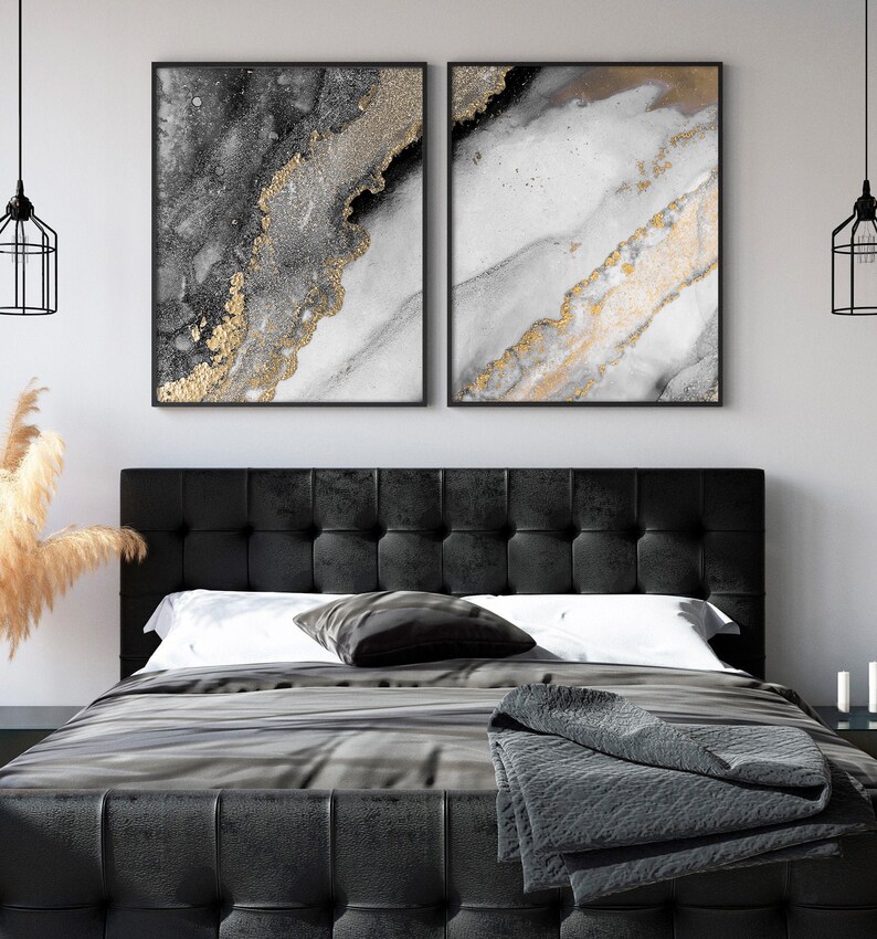 Puede incluir: Dos impresiones de arte abstracto con pintura negra, blanca y dorada. Las impresiones est&aacute;n enmarcadas en negro y colgadas en una pared blanca sobre una cabecera negra.