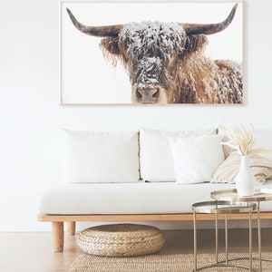 May include: A framed print of a Highland cow with snow on its fur and horns. The artwork hangs above a white sofa with cream-coloured cushions. The text "TURN YOUR TV INTO ART" and "96th AVENUE" are visible.