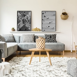 K&ouml;nnte beinhalten: Ein graues Ecksofa mit schwarz-wei&szlig;en Kissen in einem Wohnzimmer mit Kamin, Couchtisch und Teppich. An der Wand &uuml;ber dem Sofa h&auml;ngen zwei schwarz-wei&szlig;e gerahmte Drucke.