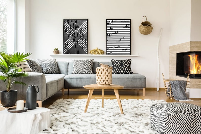 K&ouml;nnte beinhalten: Ein graues Ecksofa mit schwarz-wei&szlig;en Kissen in einem Wohnzimmer mit Kamin, Couchtisch und Teppich. An der Wand &uuml;ber dem Sofa h&auml;ngen zwei schwarz-wei&szlig;e gerahmte Drucke.