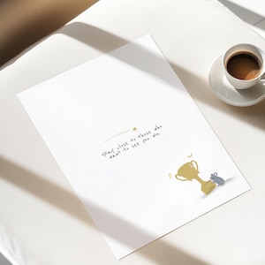 May include: A white print with the text "Stay close to those who want to see you win" and a gold trophy illustration with a gray mouse. A cup of coffee sits on a white saucer.