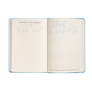Puede incluir: Un libro azul de pasaporte del Parque Nacional con una ilustraci&oacute;n de una monta&ntilde;a y &aacute;rboles en la portada. El texto "National Park Passport" est&aacute; impreso en la portada. El texto "Collect a stamp from every National Park you visit." est&aacute; impreso en la parte inferior de la p&aacute;gina derecha.
