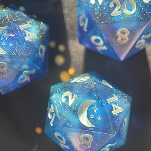 May include: A set of blue, glittery dice with white numbers and a crescent moon design. The dice are a d20, a d12, and a d8.