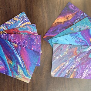 May include: A set of eight cards with abstract marbled designs in shades of purple, blue, teal, and gold. The cards have a textured, metallic finish.