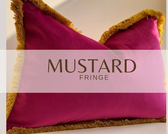 Puede incluir: Un cojín rectangular de terciopelo magenta con un borde de flecos amarillo mostaza en los cuatro lados. El texto MUSTARD FRINGE está impreso en letras de color marrón oscuro en el centro del cojín, sobre la superficie de tela magenta.