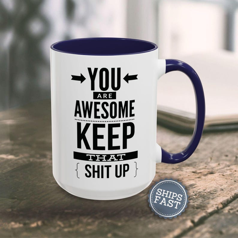 A white and blue mug with the text "YOU ARE AWESOME KEEP THAT SHIT UP" printed on it, along with two arrows pointing to the mug.