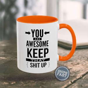 An orange and white coffee mug with the text "YOU ARE AWESOME KEEP THAT SHIT UP" printed on it.