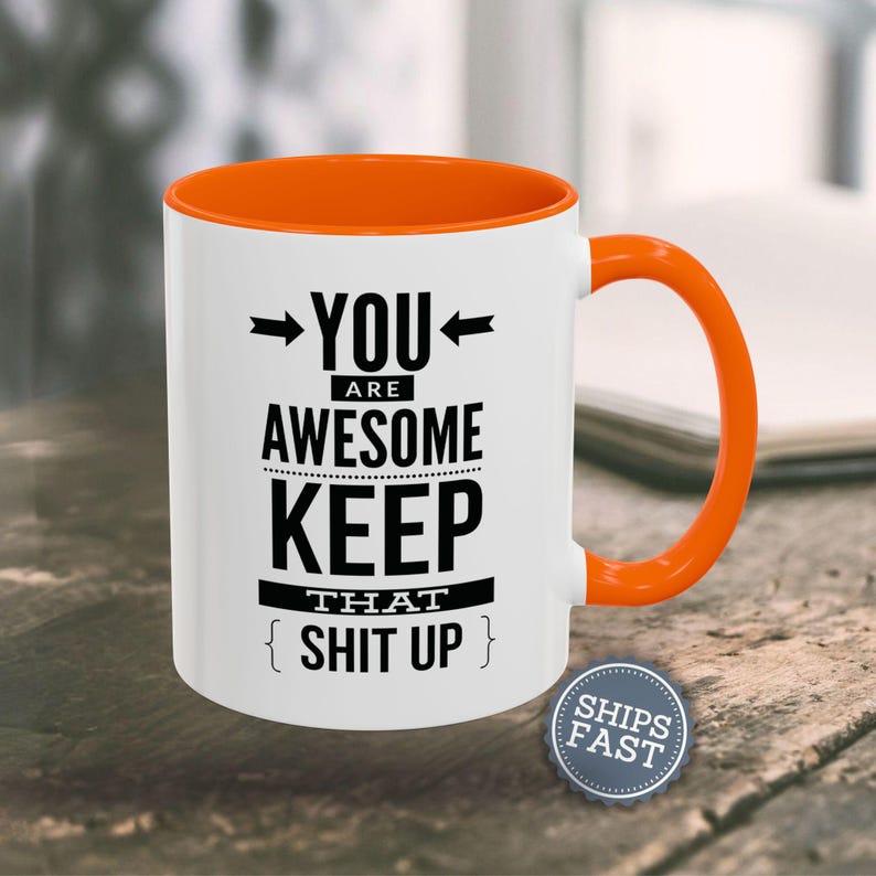 An orange and white coffee mug with the text "YOU ARE AWESOME KEEP THAT SHIT UP" printed on it.