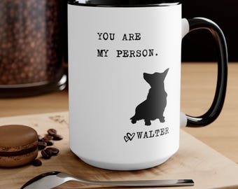Puede incluir: Taza de cerámica blanca con interior y asa negros. La taza presenta el texto "YOU ARE MY PERSON." encima de una silueta negra de un perro y el nombre "WALTER" con un símbolo de corazón. Una cuchara y un pastel están en primer plano.