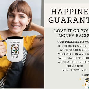 May include: White ceramic mug with a black interior, featuring a cartoon cat design and the text "SHOPPY-GO-LUCKY". The mug also includes the text "HAPPINESS GUARANTEE" and "LOVE IT OR YOUR MONEY BACK!"