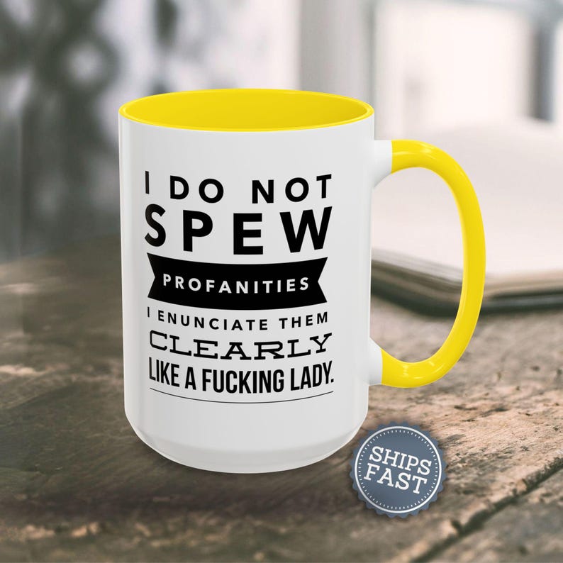 A white coffee mug with a yellow handle, featuring a humorous text that reads "I DO NOT SPEW PROFANITIES I ENUCIATE THEM CLEARLY LIKE A FUCKING LADY."