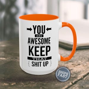 A white and orange mug with the text "YOU ARE AWESOME KEEP THAT SHIT UP" printed on it, along with two arrows pointing to the mug.