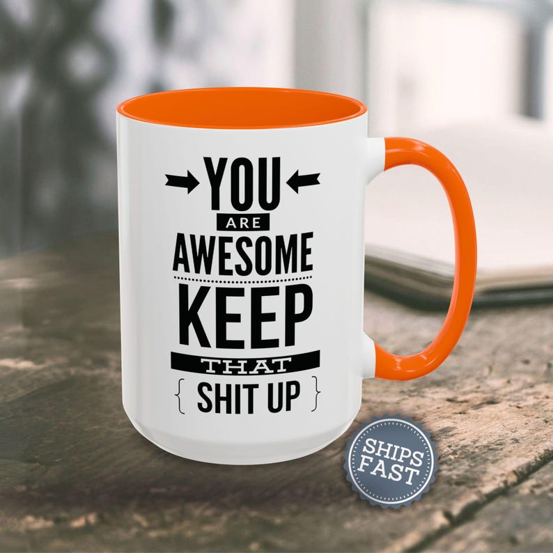 A white and orange mug with the text "YOU ARE AWESOME KEEP THAT SHIT UP" printed on it, along with two arrows pointing to the mug.