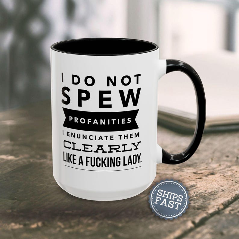 A white coffee mug with black text and a black handle, placed on a wooden surface.