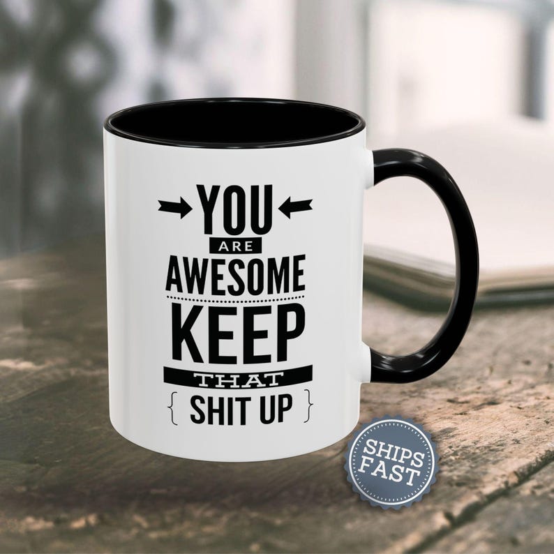 A white coffee mug with black text and graphics on it, placed on a wooden surface.