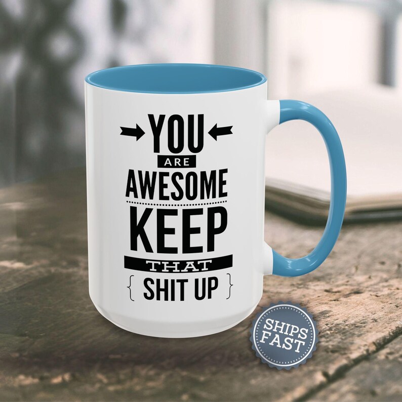 A white and blue mug with the text "YOU ARE AWESOME KEEP THAT SHIT UP" printed on it, along with a blue handle.
