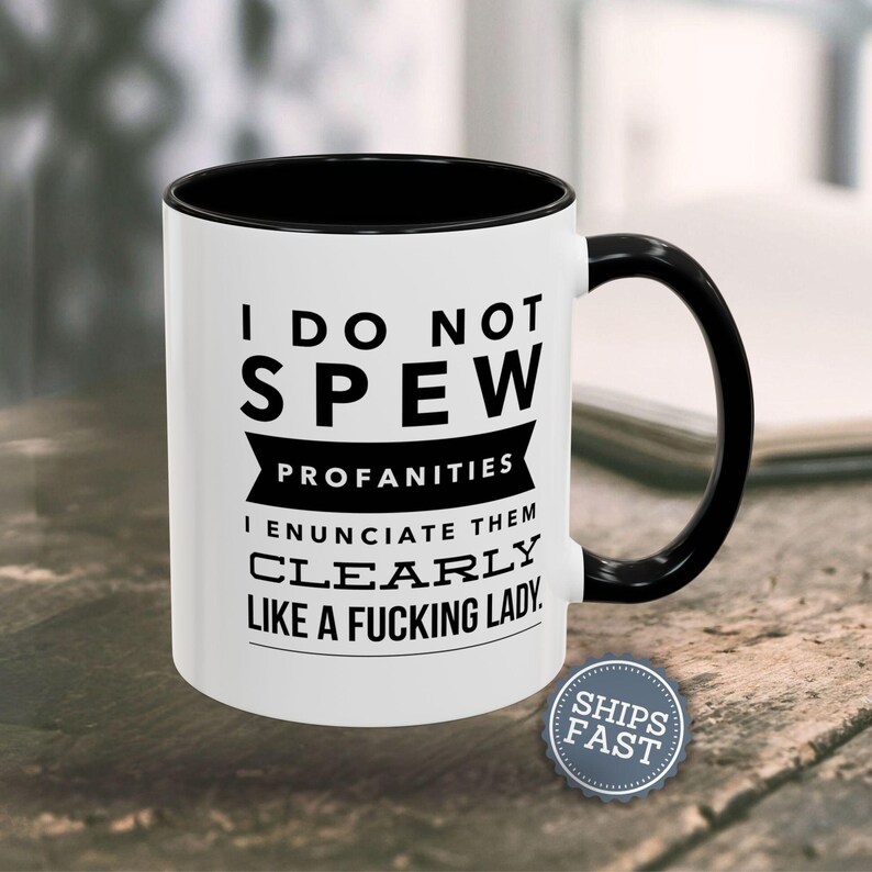 A white coffee mug with black text and a black handle, placed on a wooden surface.