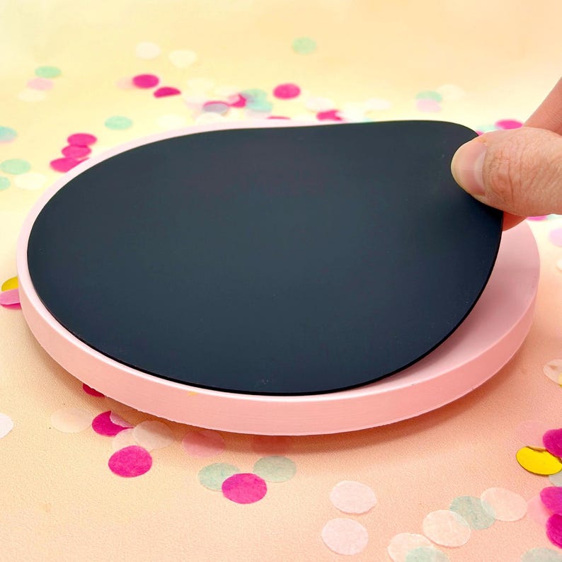 Pode incluir: Um prato girat&oacute;rio redondo rosa com uma parte superior circular preta remov&iacute;vel. O prato girat&oacute;rio est&aacute; sobre uma superf&iacute;cie com confete.
