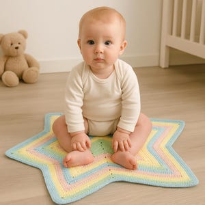 May include: A baby sits on a pastel-colored star-shaped crochet blanket. The blanket features a blue border and a pattern of yellow, pink, and green stripes. The baby wears a white onesie and looks directly at the camera.