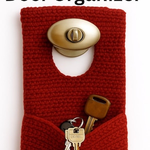 May include: A red crocheted door organiser with a pocket, holding keys. The organiser hangs from a brass-coloured door handle. Text at the top reads "Crochet Door Organizer".